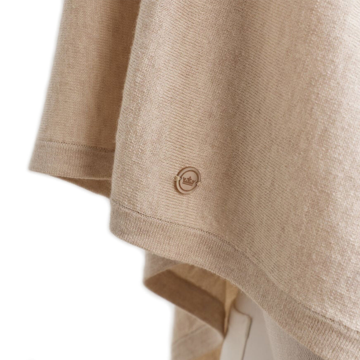 Close-up of the hem on the Peter Millar Boeing Women’s Spring Blend Poncho by BOEING, showing its beige cotton-silk-cashmere blend and a small crown logo near the edge. The lightweight fabric is soft and drapes loosely.