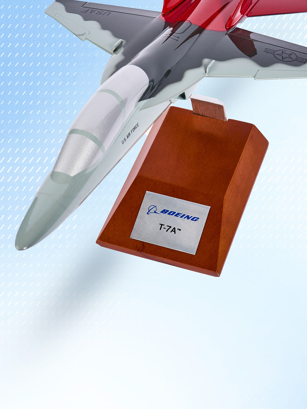Model of a Boeing T-7A aircraft on a wooden display stand with a blue gradient background.