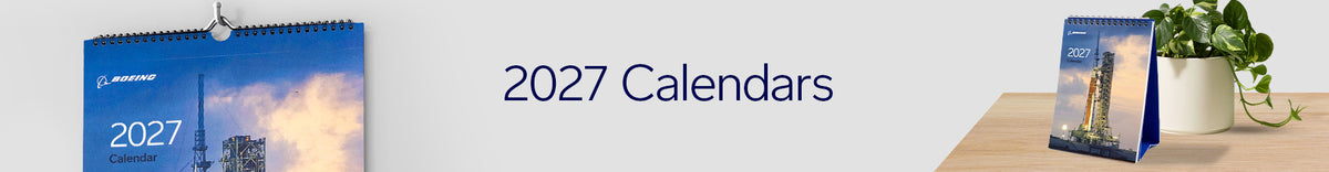 Two Boeing 2027 calendars, one wall-mounted and one standing on a desk next to a potted plant.