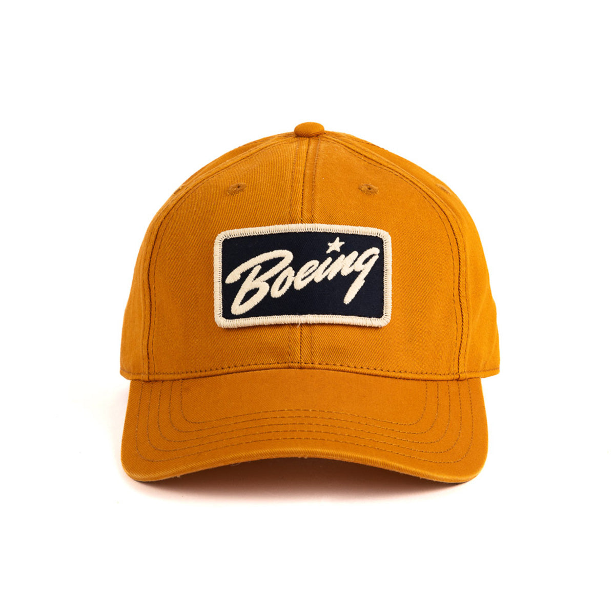 The Boeing Stores Boeing Washed Twill Patch Hat is a mustard-yellow baseball cap with a curved brim, showcasing an embroidered patch that reads Boeing in white on black. It features the Boeing script logo and has an adjustable buckle closure for a perfect fit.