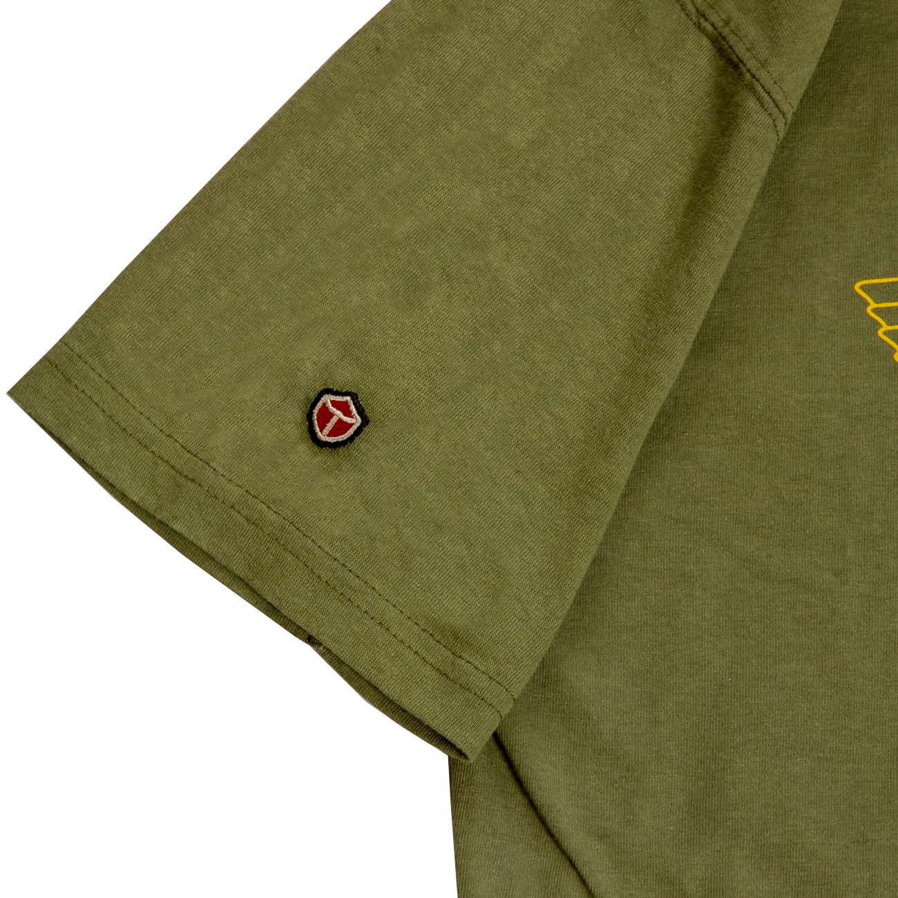 The Boeing Stores Red Canoe Boeing Airplane Company Logo T-Shirt features an olive green sleeve with a red and black embroidered shield logo. Made from 100% cotton, it includes subtle stitching and a partial yellow graphic reminiscent of vintage Boeing designs.