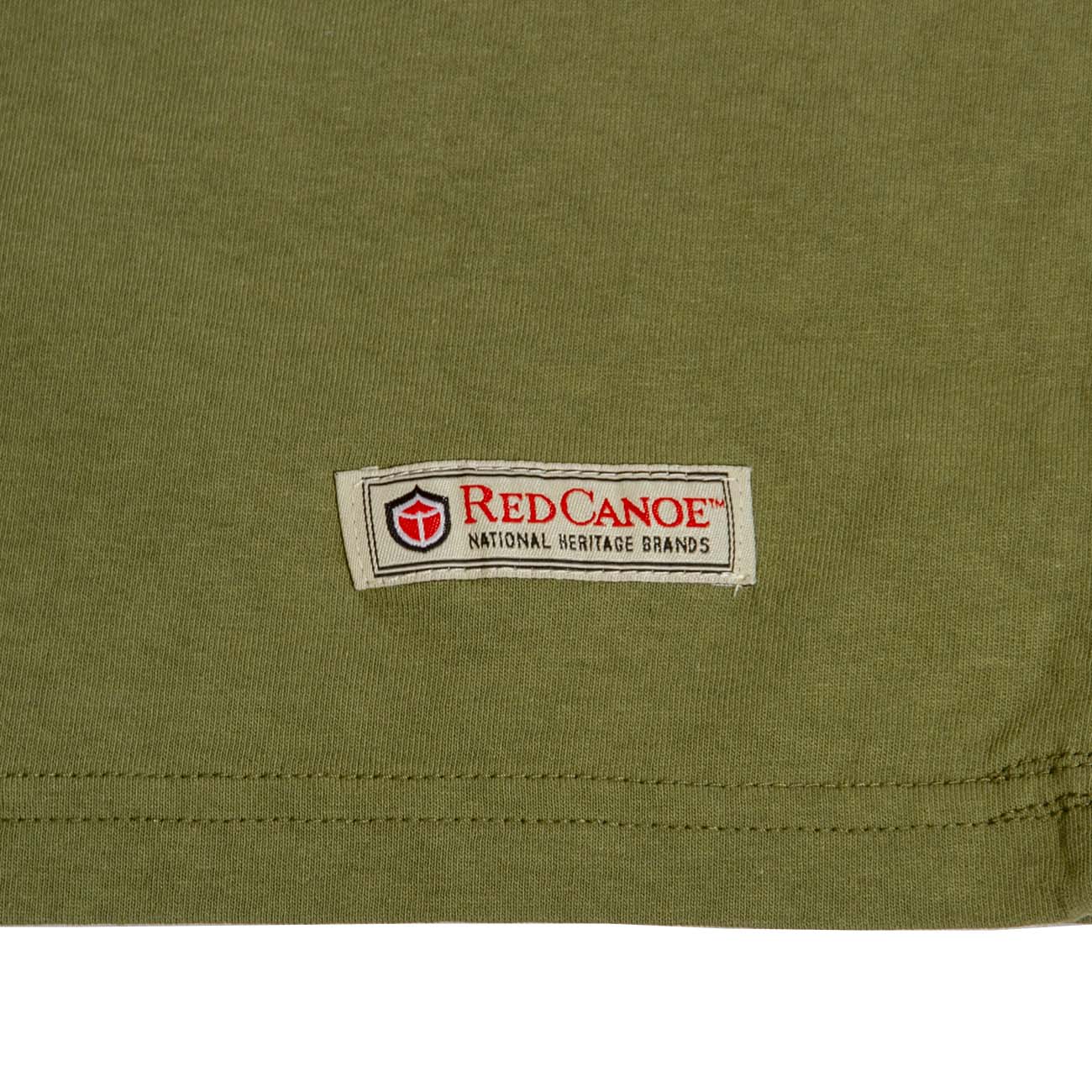 A close-up of an olive-green fabric shows a rectangular patch with a red and black shield logo, the text Red Canoe National Heritage Brands, and tributes to Boeings legacy—a perfect touch for The Boeing Store’s Red Canoe Boeing Airplane Company Logo T-Shirt in any retro tee collection.