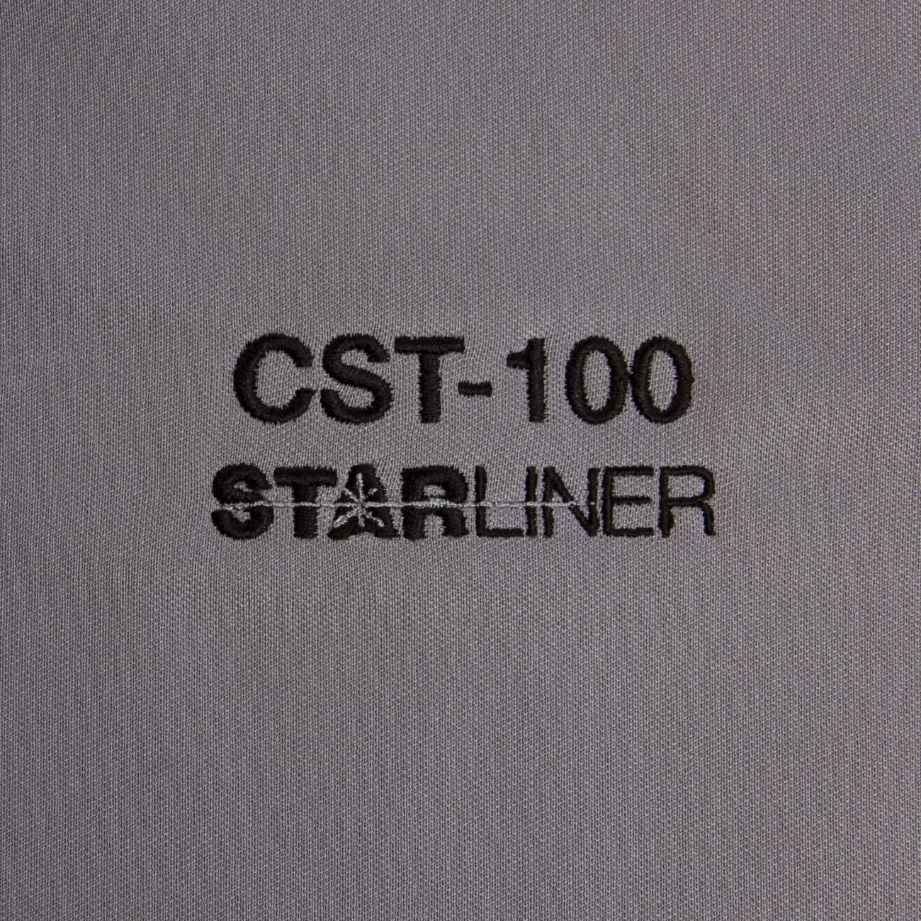Close-up of gray fabric with Boeing Starliner CST-100 embroidered in black text, highlighting The Boeing Stores innovative design. Perfect for your moisture-wicking polo collection.