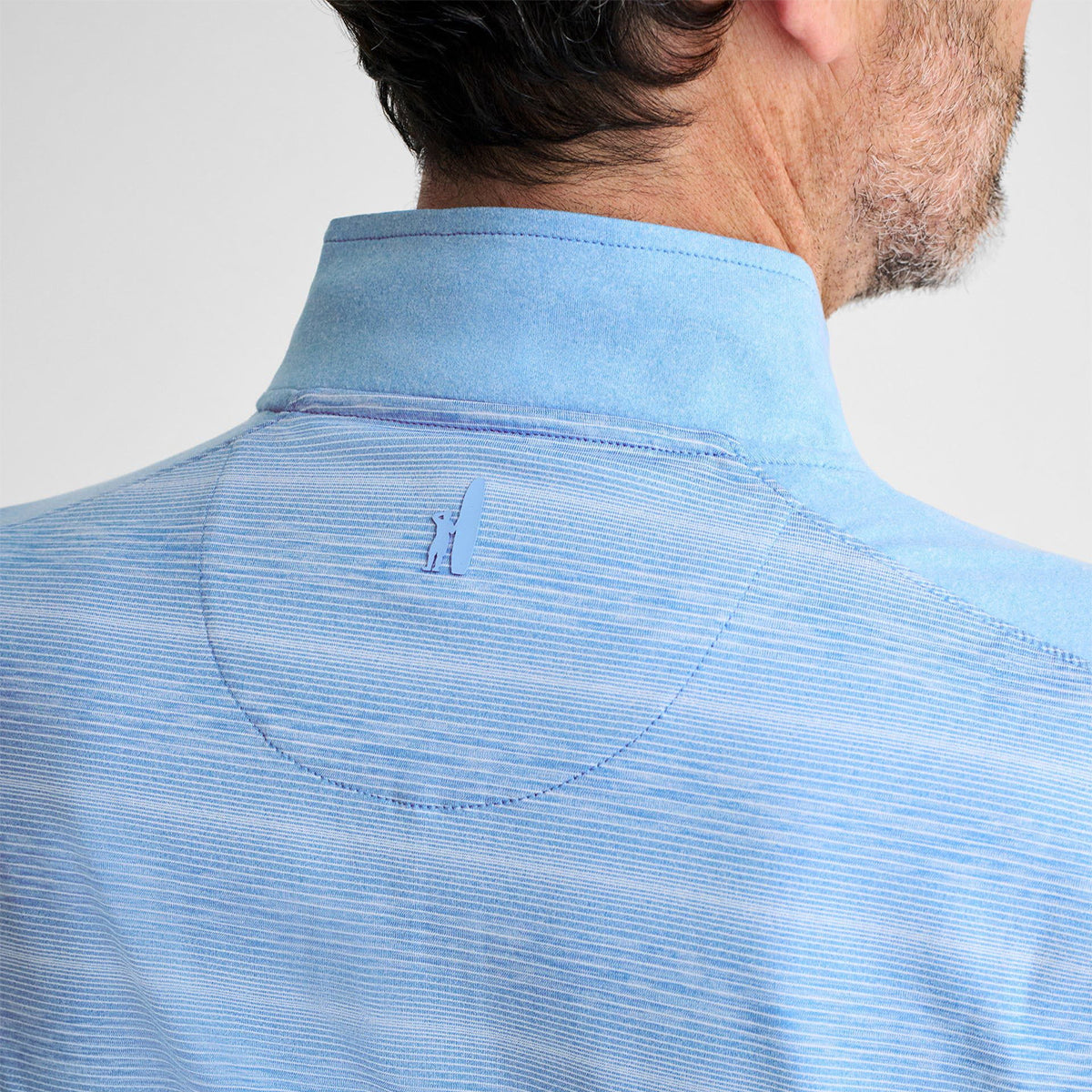 A person is seen from the back wearing a light blue johnnie-O Boeing Mens Bert Quarter-Zip Pullover, featuring subtle horizontal stripes and a sailboat logo at the upper back. Made with moisture-wicking technology, it highlights their short dark hair and part of their neck.