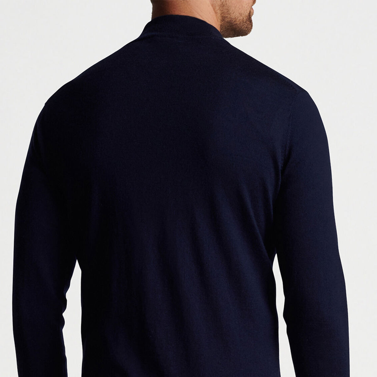 A man is seen from behind wearing a dark navy Peter Millar Boeing Mens Autumn Crest Quarter-Zip sweater by The Boeing Store, made from luxurious Merino wool. The plain, light-colored background highlights the garments elegance.