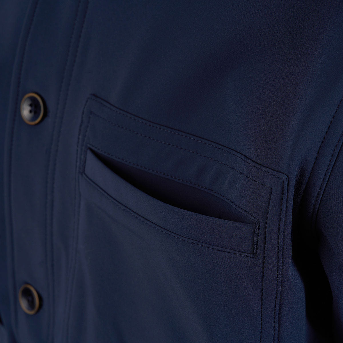Close-up of The Boeing Store’s Mens Tech Modern Chore Jacket in navy blue, featuring black buttons and a flap chest pocket. The smooth, matte fabric enhances the jacket’s modern look.