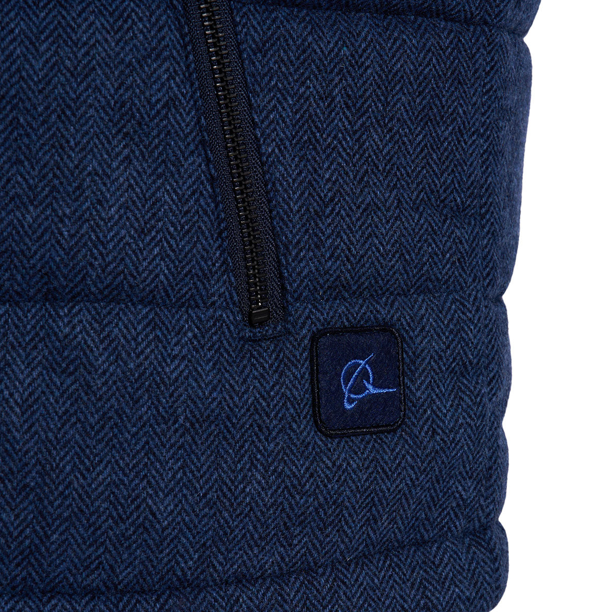 Close-up of Boeing Mens Wool Blend Quilted Vest by The Boeing Store: blue herringbone fabric, polyester padding, vertical black zipper, and a small patch with an embroidered light blue narwhal logo—ideal for winter style.