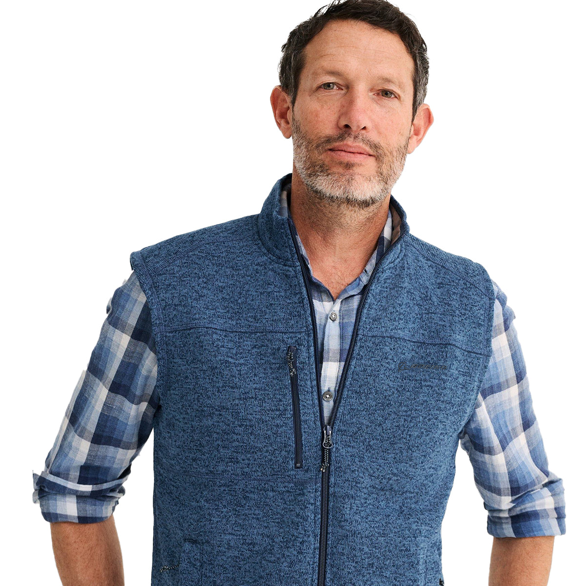 A man with short hair and a beard is wearing a blue plaid shirt and a sleeveless johnnie-O Boeing Mens Wes Fleece Vest from The Boeing Store. He stands against a plain white background, looking at the camera with a neutral expression.