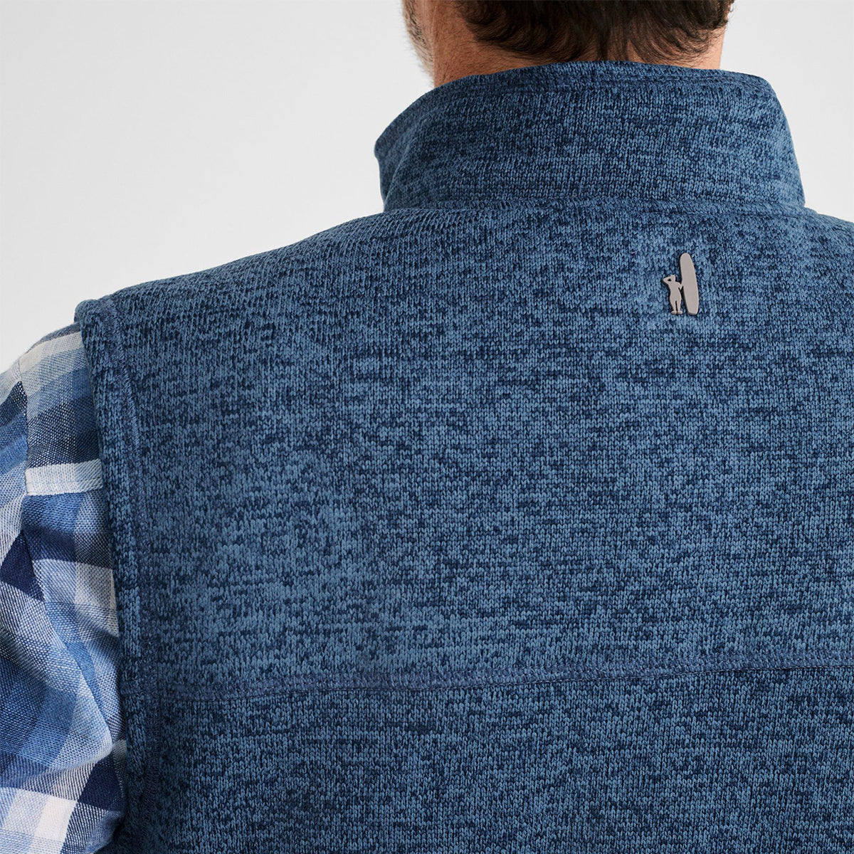 A person wearing a blue textured johnnie-O Boeing Mens Wes Fleece Vest from The Boeing Store over a blue and white plaid shirt, seen from the back. The vest includes a small logo near the collar, ideal for style seekers, with no returns on this unique clearance item.