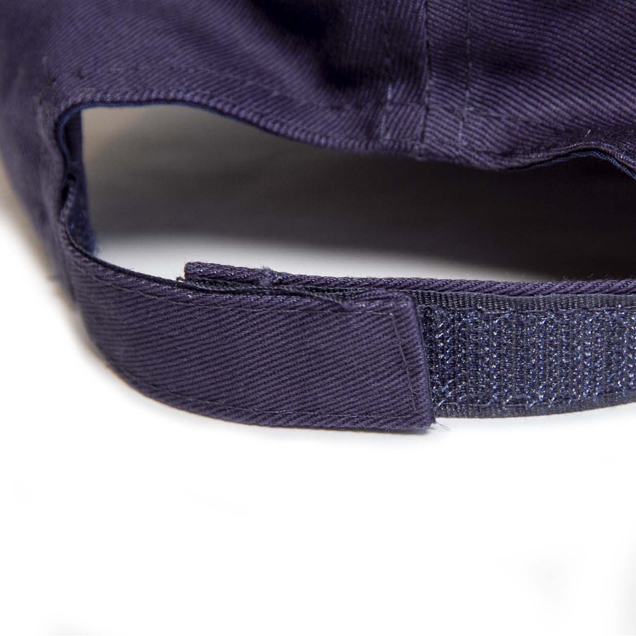 Close-up of the back of The Boeing Stores Boeing 787 Hat in navy blue reveals an adjustable Velcro closure. Made from 100% cotton, the image emphasizes its classic look and fastening mechanism against a light background.
