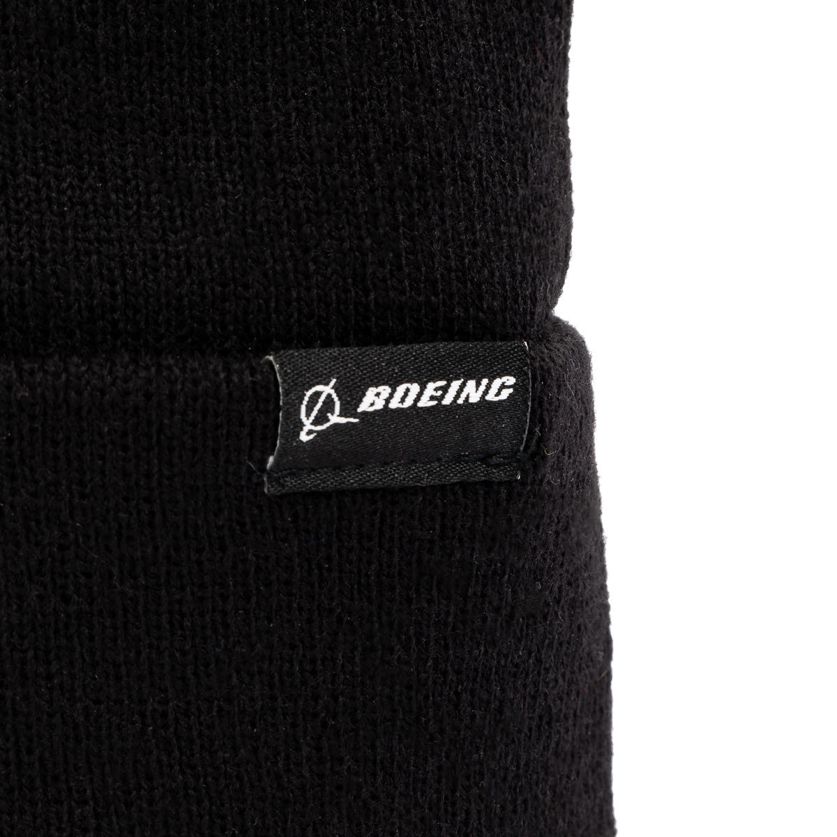 Close-up of The Boeing Store’s Boeing Signature Logo Beanie, a black knit hat with a small black tag displaying the Boeing logo and “BOEING” in white.