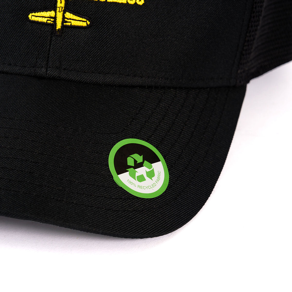 Close-up of the Boeing B-17 Flying Fortress Heritage Hat by The Boeing Store, featuring a green sticker on the brim with a white recycling symbol and 100% RECYCLED COTTON text, plus partially visible yellow embroidery.
