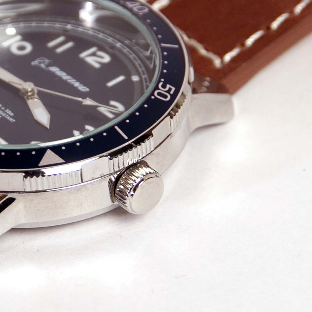 The Boeing Stores Boeing Brown Leather Watch features a stainless steel case, blue bezel, Japanese movement, and water resistance. It has white numerals on its dial and a crown on the right side. The close-up highlights its brown leather strap alongside detailed side and bezel designs.