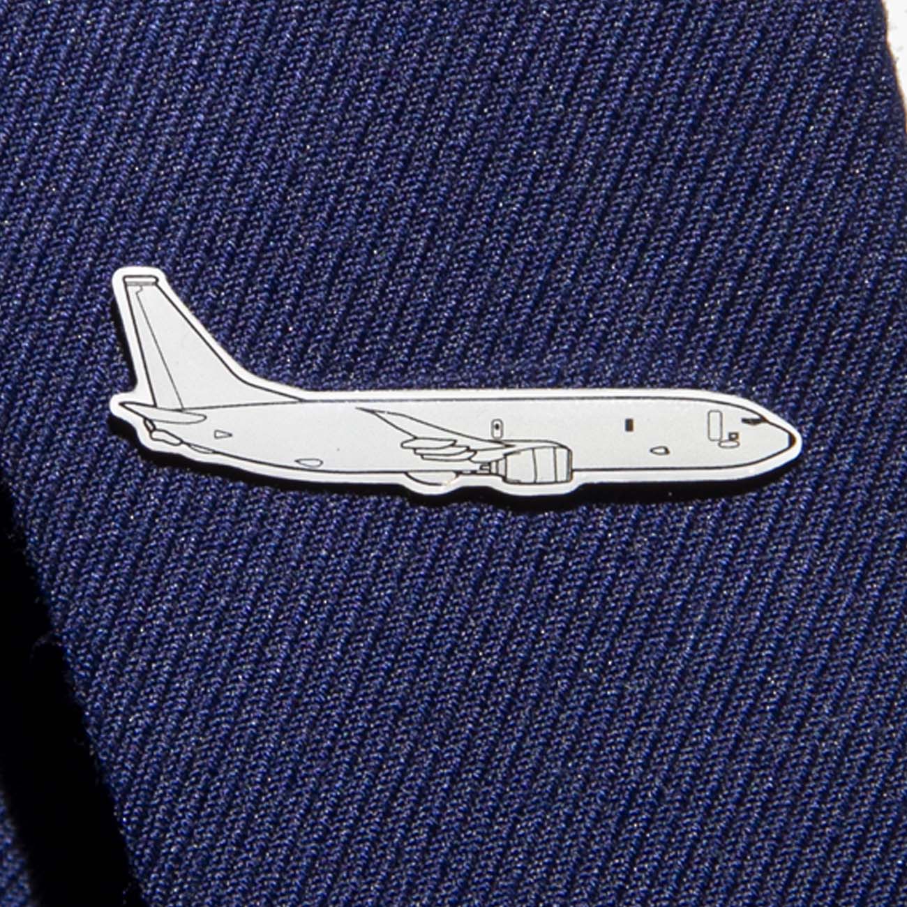 The Boeing Illustrated P-8 Lapel Pin from The Boeing Store is a silver-tone pin shaped like a jet, attached to dark blue textured fabric, subtly echoing the sleek design of the Boeing logo.