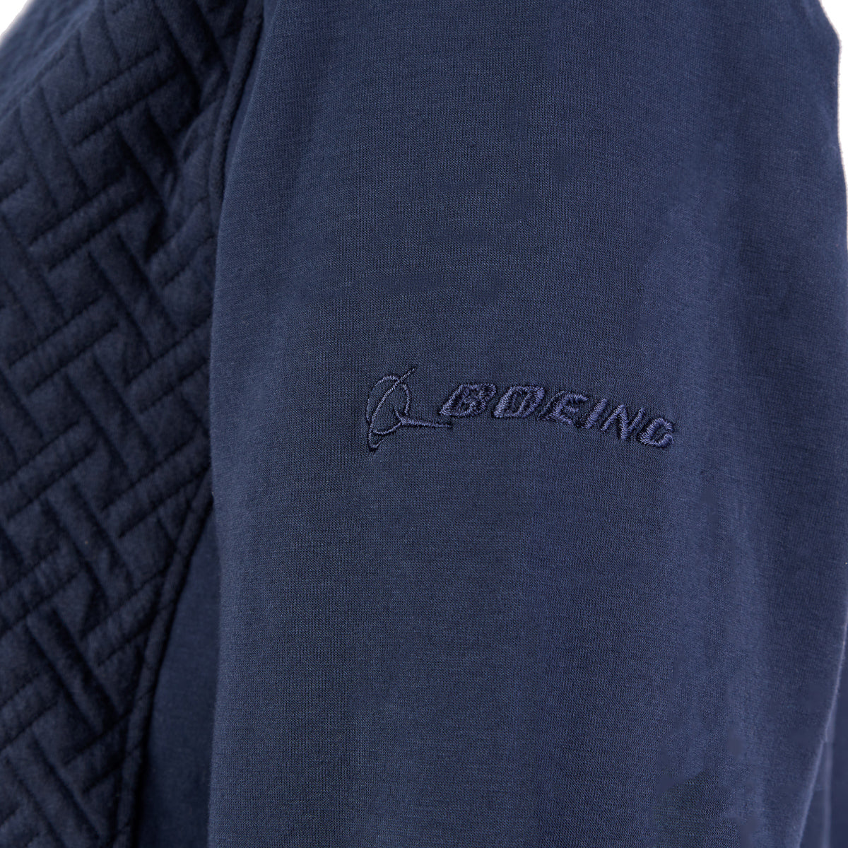 The Boeing Store’s Signature Logo Womens Quilted Full-Zip showcases a navy blue ladies cut, quilted shoulders, and a matching blue embroidered Boeing logo on the sleeve, crafted from soft-hand knit fabric for comfort.