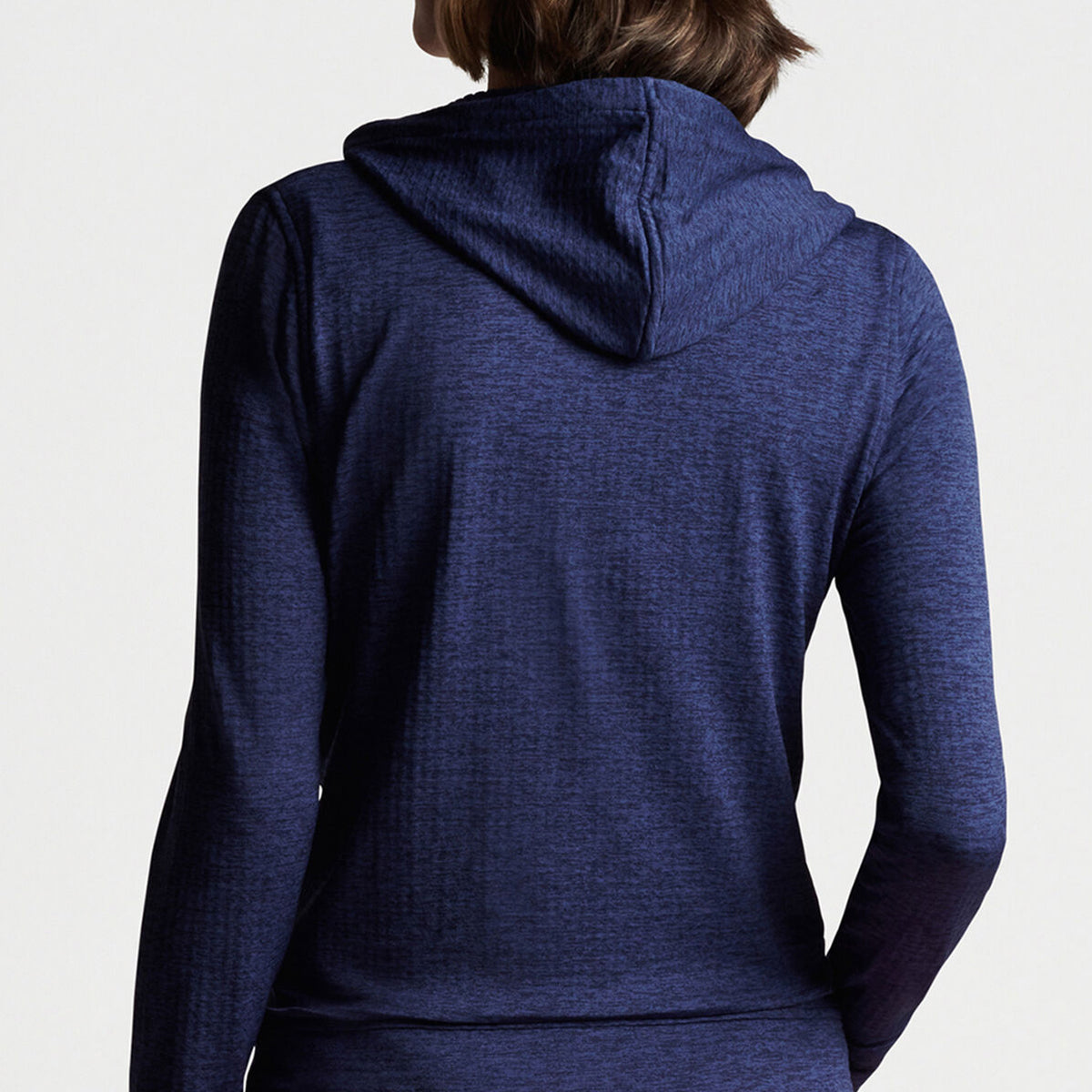 A person showcases the Peter Millar Boeing Women’s French Terry Full-Zip Hoodie from The Boeing Store, revealing the navy blue performance fabric and textured material. The hood is down, enhancing its moisture-wicking design against a plain white background with their short brown hair visible.
