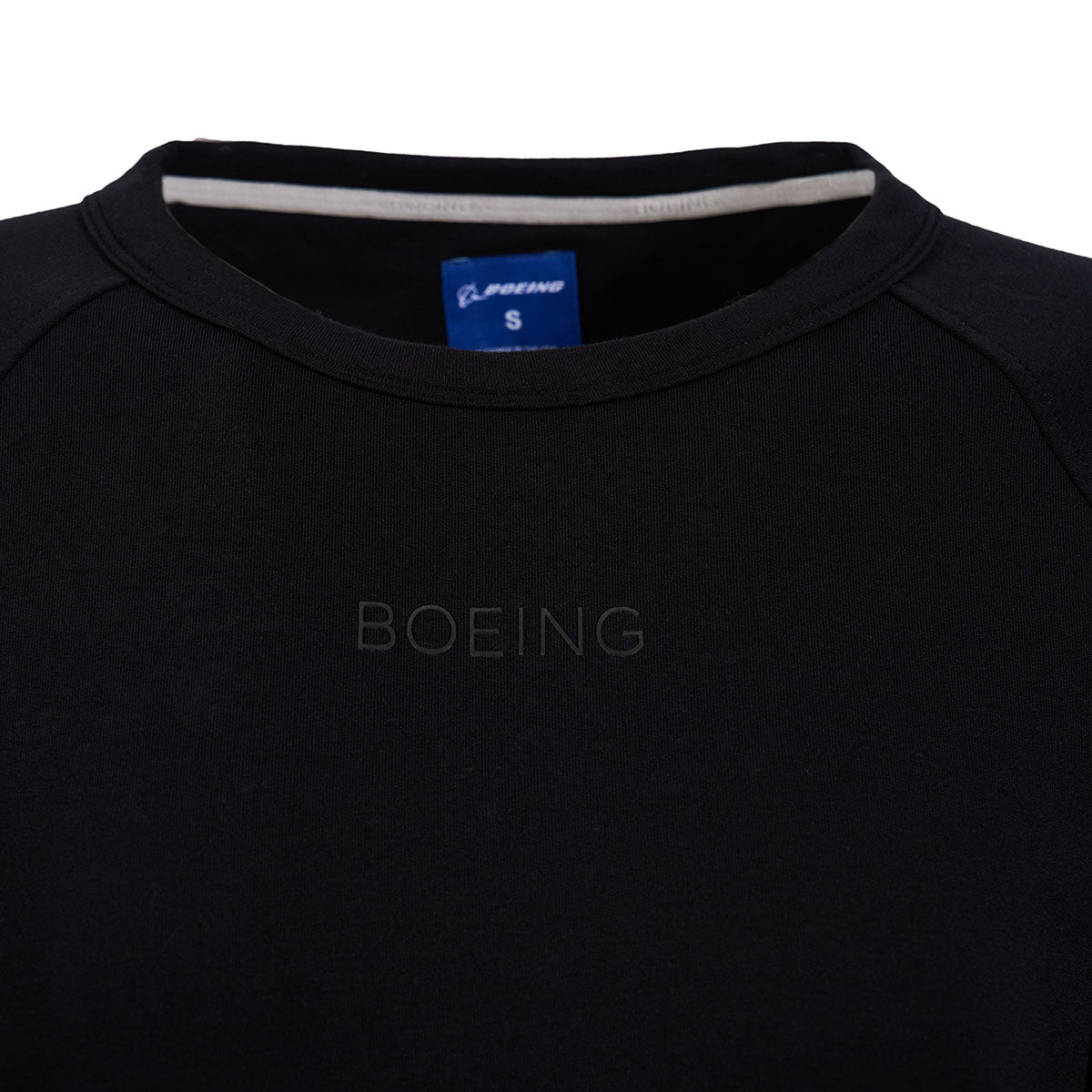 A close-up of a black crewneck features a subtle BOEING silicone patch. The inner label shows its an ALPINE PRO, size S, crafted from a cotton blend for comfort. This is the Boeing Womens Raglan Crewneck Sweatshirt by The Boeing Store.