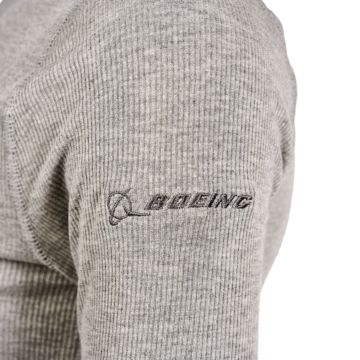 Close-up of a persons arm wearing the Glyder Boeing Womens Ruby Mock-Neck Long-Sleeve from The Boeing Store, featuring a textured gray design with an embroidered black Boeing logo on the sleeve.