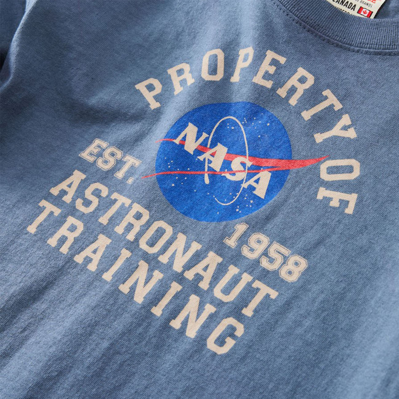 Close-up of The Boeing Stores Red Canoe Boeing Kids NASA Astronaut T-Shirt with the iconic logo and text Property of ASTROnaut Training Est. 1958. Laid flat, it showcases a vibrant design perfect for young space enthusiasts.