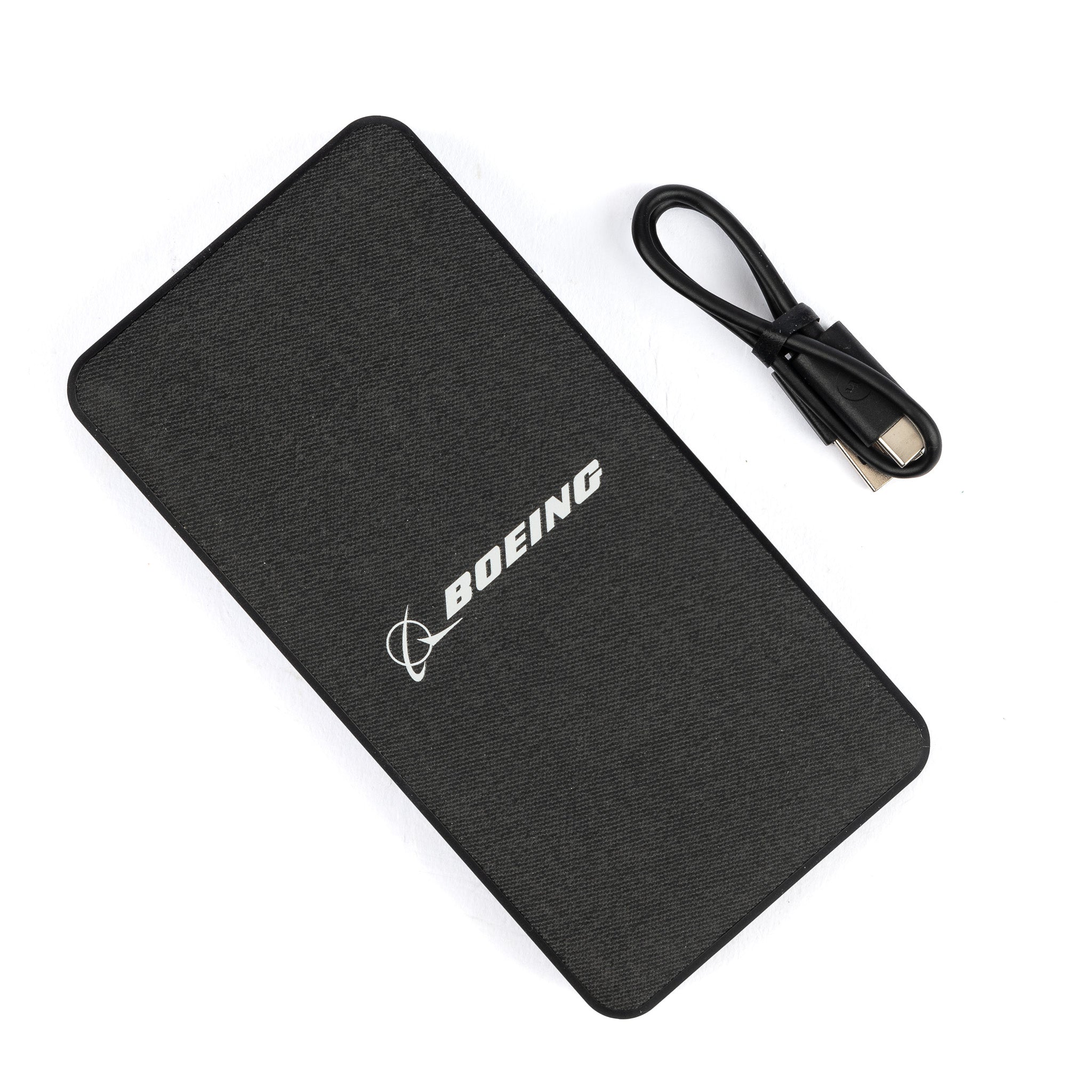 The Mophie Boeing Powerstation XXL Power Bank from The Boeing Store, featuring the Boeing logo, has a black textured surface for enhanced grip, a 20,000mAh capacity, two USB ports for versatile charging, and sits beside a coiled USB cable.