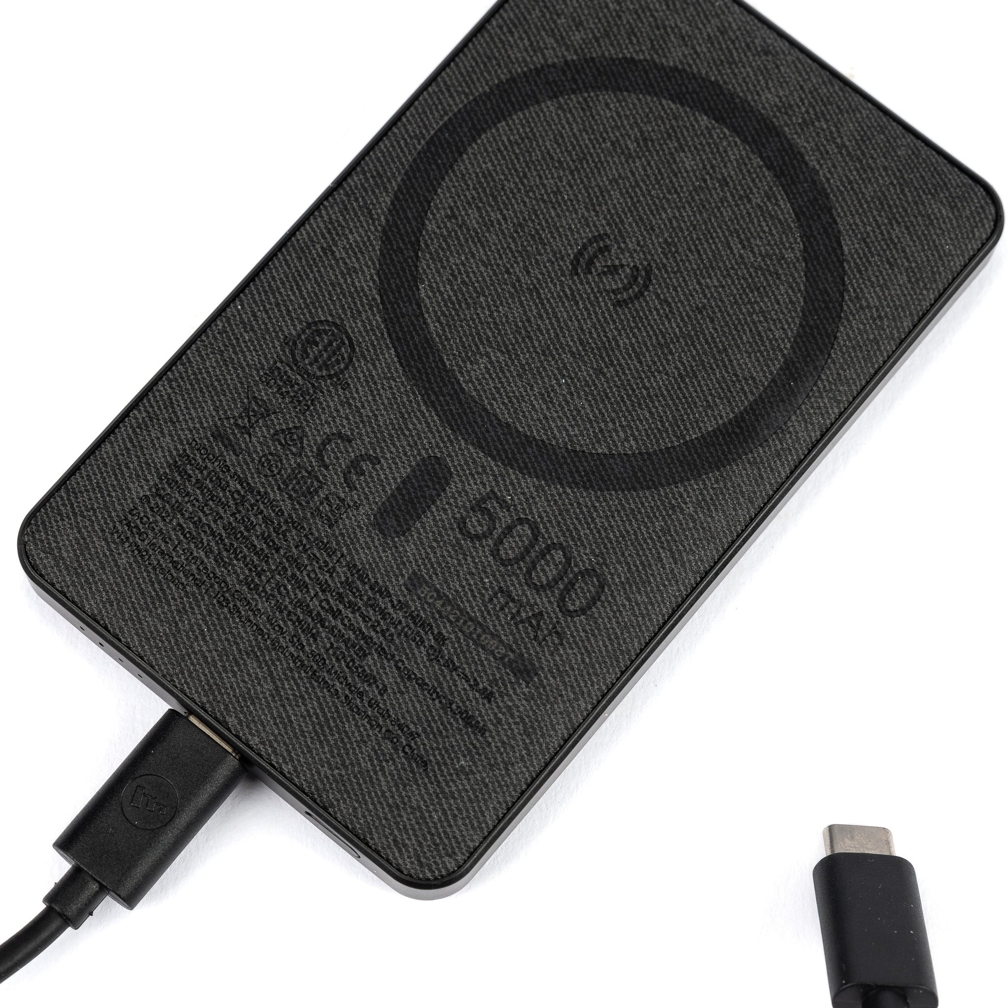 The Mophie Boeing Snap+ Juice Pack Mini Power Bank by The Boeing Store is a sleek black portable wireless charger with a round charging symbol, connected to a USB-C cable. Its MagSafe compatible, labeled with technical specs and compliance symbols. A nearby disconnected USB-C plug is visible.