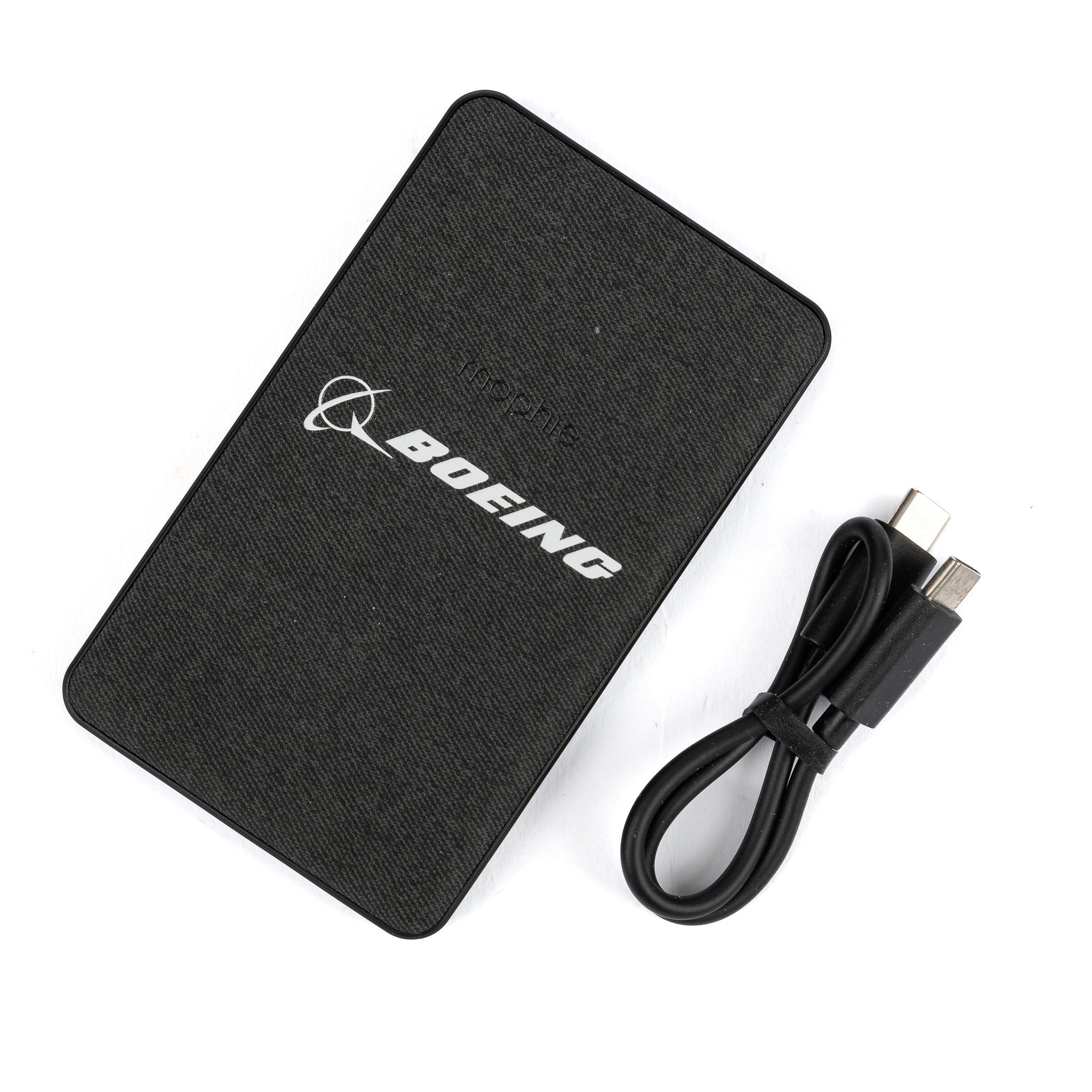 Beside a coiled USB cable, the black Boeing-branded external hard drive exudes sleek sophistication. Its textured surface and branded logo complement the Mophie Boeing Snap+ Juice Pack Mini Power Bank from The Boeing Store for seamless tech integration.