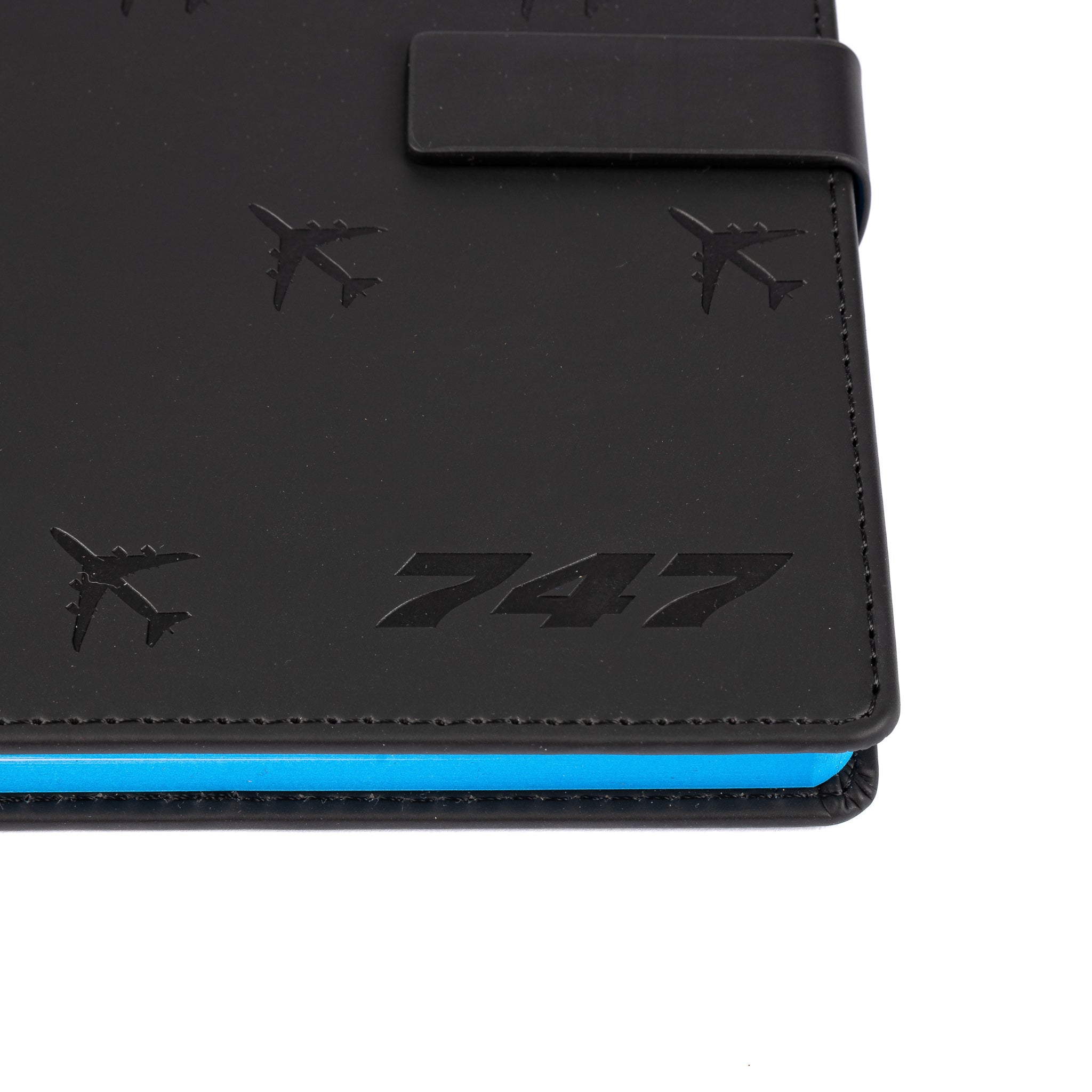 A close-up of The Boeing Store’s Boeing 747 Notebook, featuring embossed aircraft silhouettes and 747 on its black PU hardcover, with blue page edges and a magnetic flap closure.