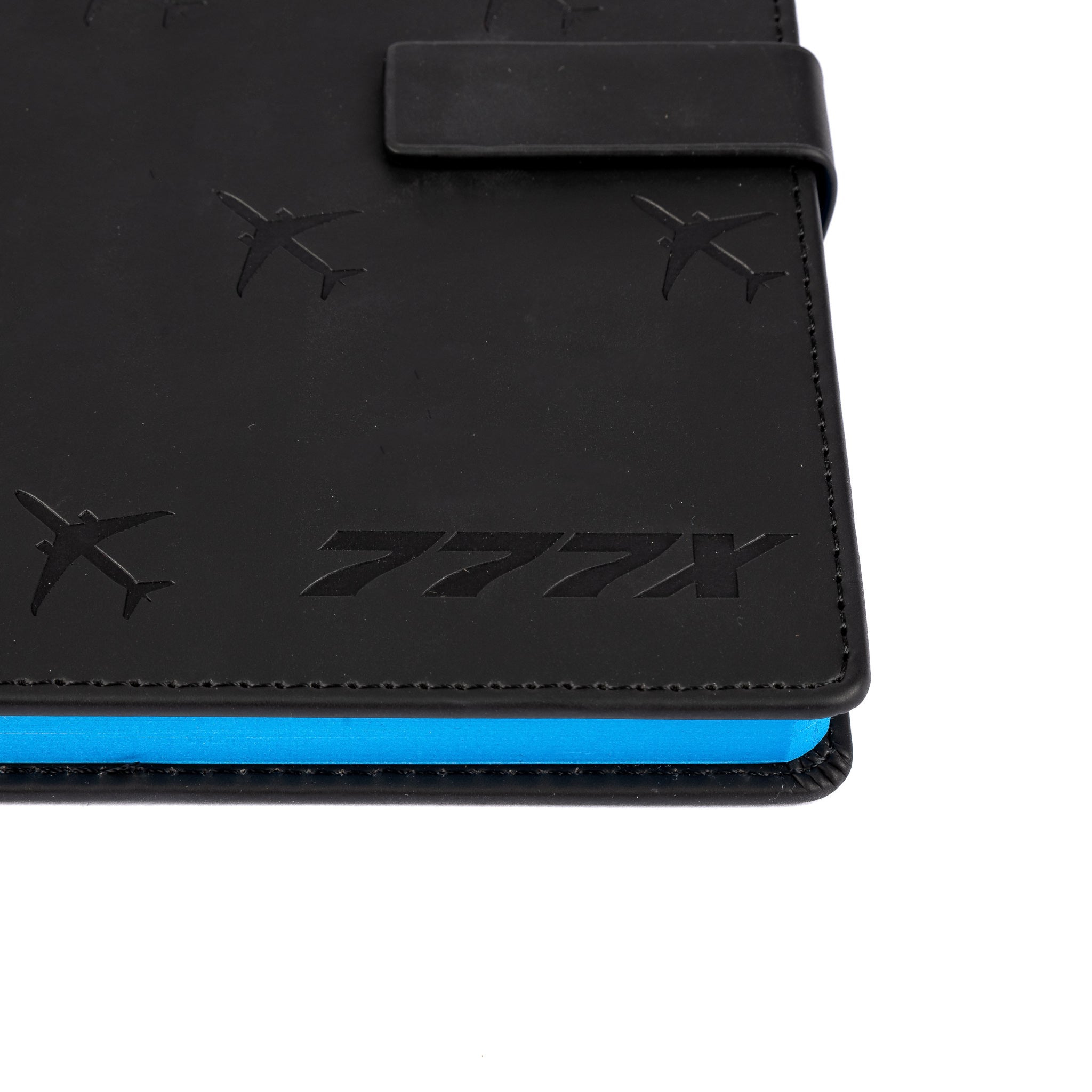 The Boeing Store’s Boeing 777X Notebook features a black cover with a debossed airplane pattern, “777X” embossed on the front, and blue-edged pages.