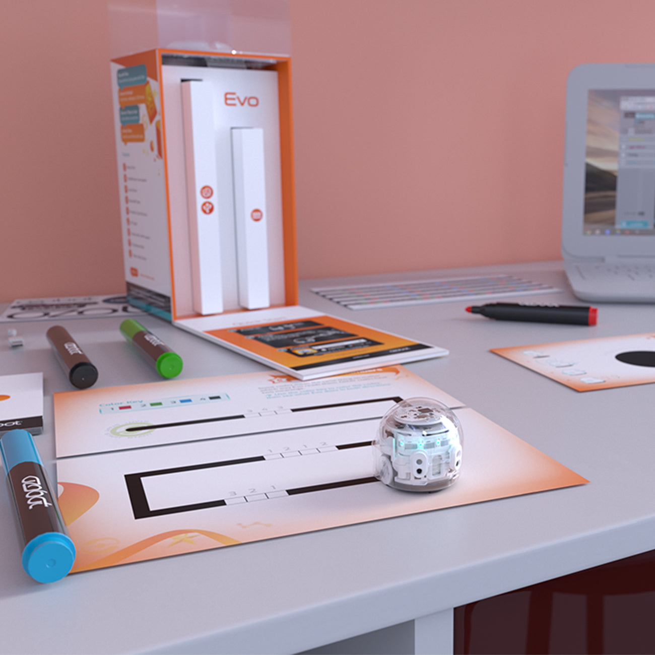 An Ozobot Evo, branded by The Boeing Store, sits on a table with a maze worksheet and colored markers. In the background, a laptop displays the Evo app and an Evo box against a peach wall, highlighting the robots OzoBlockly programming capabilities.