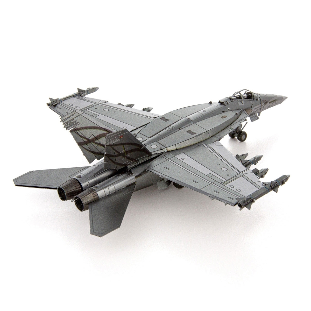 The Boeing Store’s Metal Earth Boeing F/A-18 Super Hornet, a gray twin-engine tactical aircraft with swept wings and multiple missiles under its wings, is displayed from a rear-side angle against a white background.