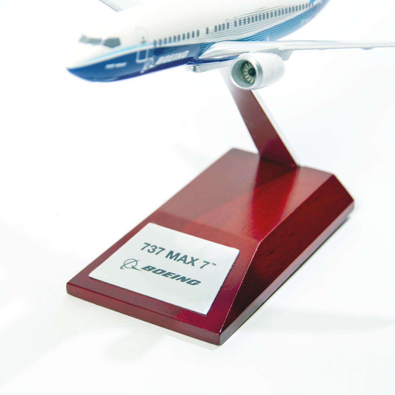 The Boeing Stores Boeing Unified 737 MAX 7 1:200 Model features a sleek fuselage placed on a wooden stand, adorned with the Boeing logo. It highlights its renowned fuel efficiency in aviation with a prominently displayed single engine.