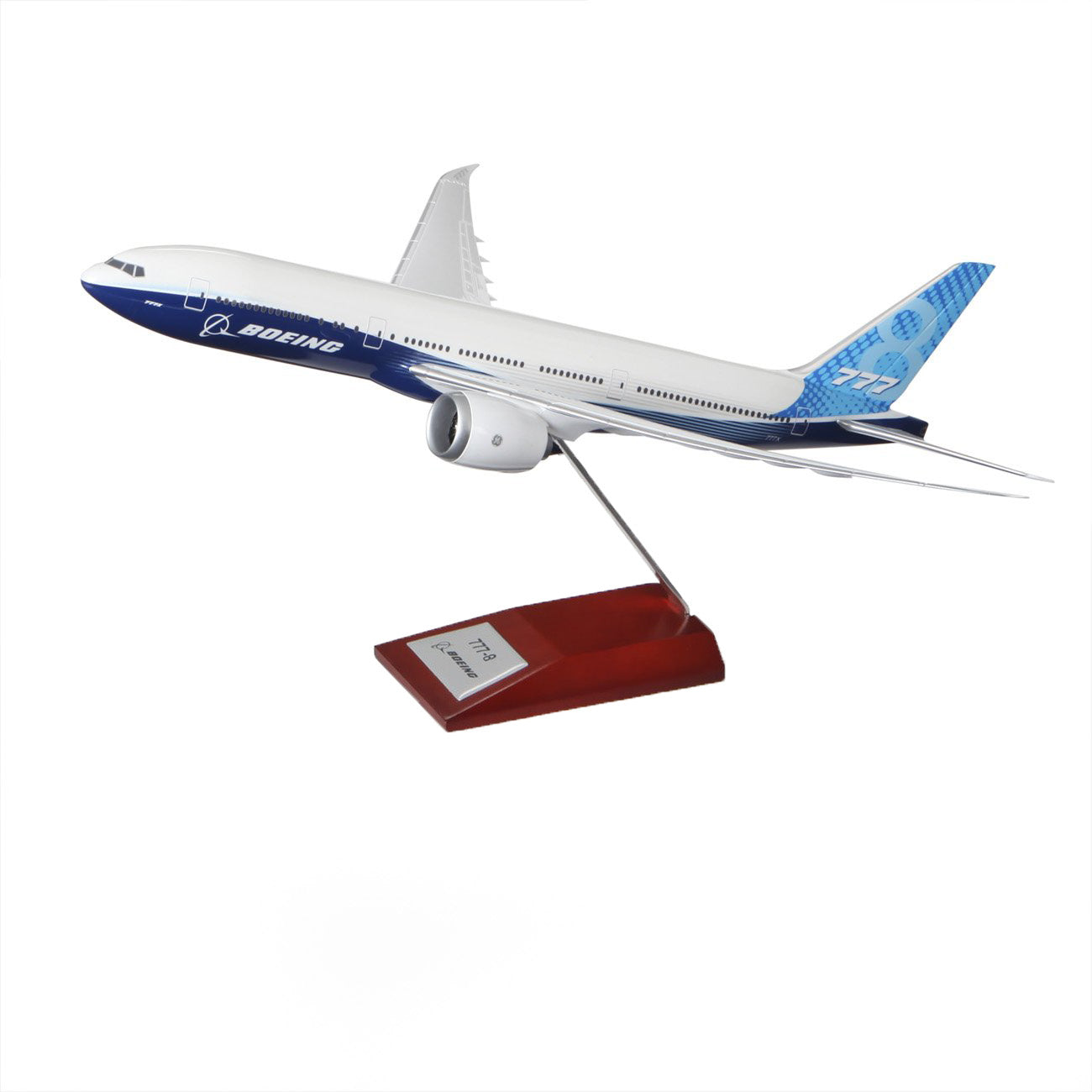 The Boeing Stores 1:200 Boeing Unified 777-8 Plastic Model, mounted on a metal rod with a wooden base, is ideal for aviation enthusiasts. It showcases the iconic Boeing house colors, with its white body, blue accents, and 777-8 model insignia elegantly displayed at the rear.