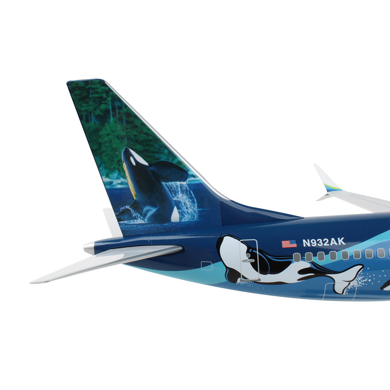A close-up of the Daron Alaska Airlines Boeing 737 MAX 9 1:100 Model shows a painted orca leaping from water on the tail, a forest background, and another orca on the fuselage. The registration number is N932AK.