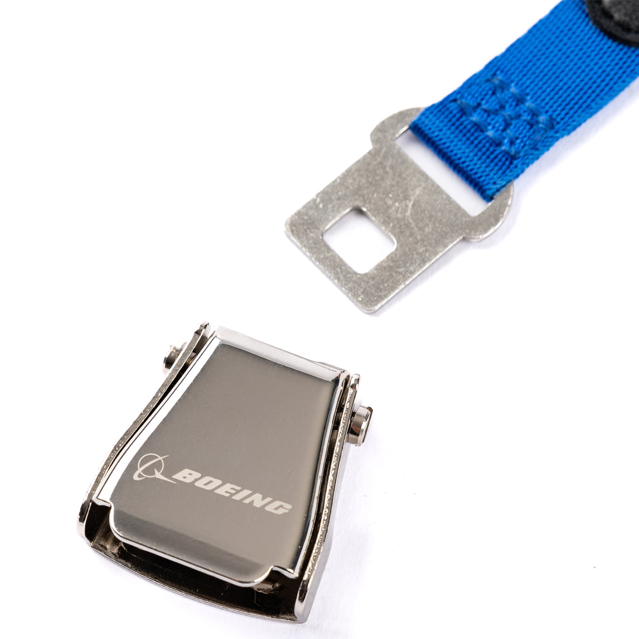 A close-up of The Boeing Store’s Boeing Seat Belt Keychain—a silver mini buckle with Boeing logo on a blue strap with metal end—perfect for airplane enthusiasts, displayed against a white background.