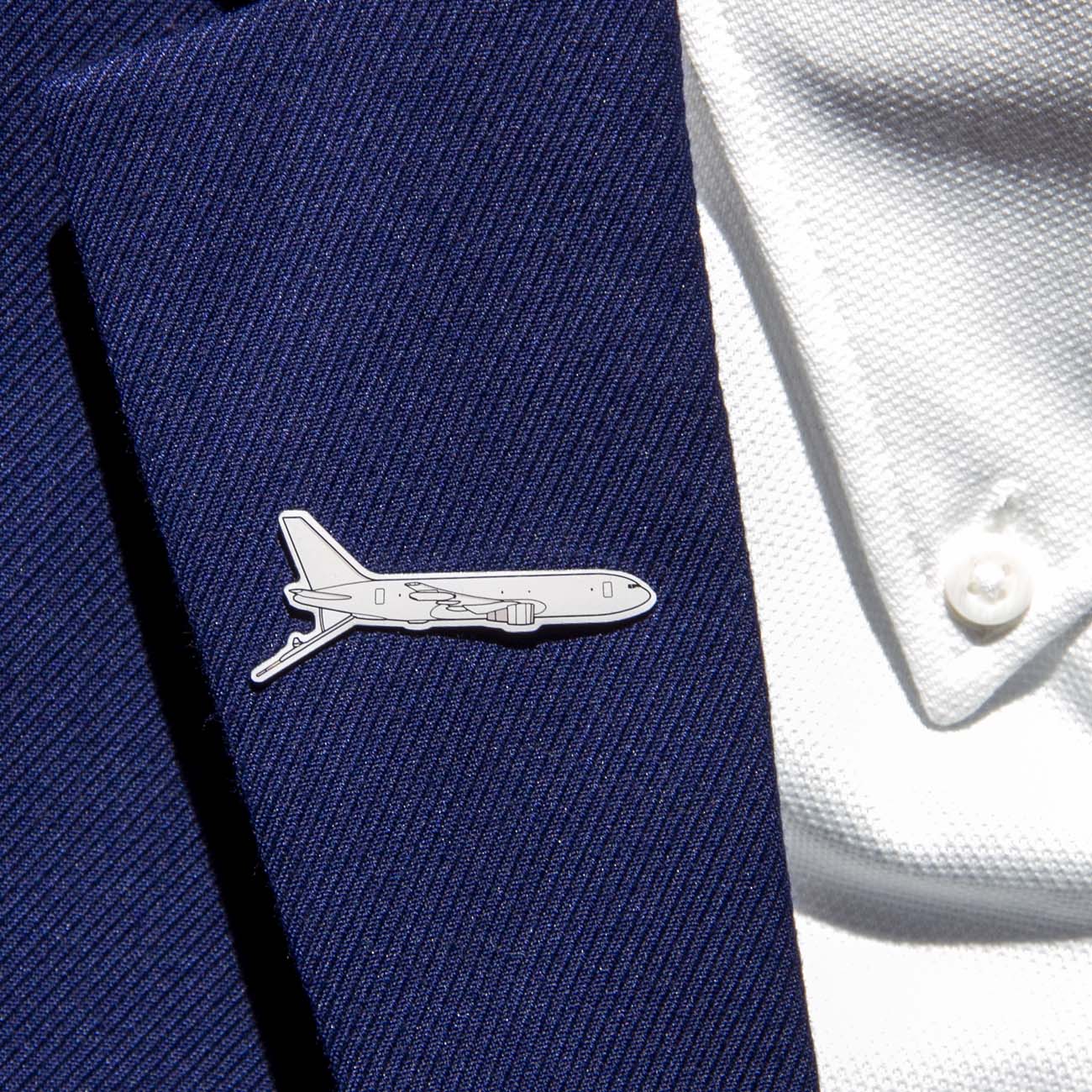 The person wears a navy blue suit jacket and white shirt, showcasing The Boeing Stores Illustrated KC-46 Lapel Pin. The silver tone pin, shaped like an airplane with the Boeing logo, subtly adorns the fine-textured fabric.