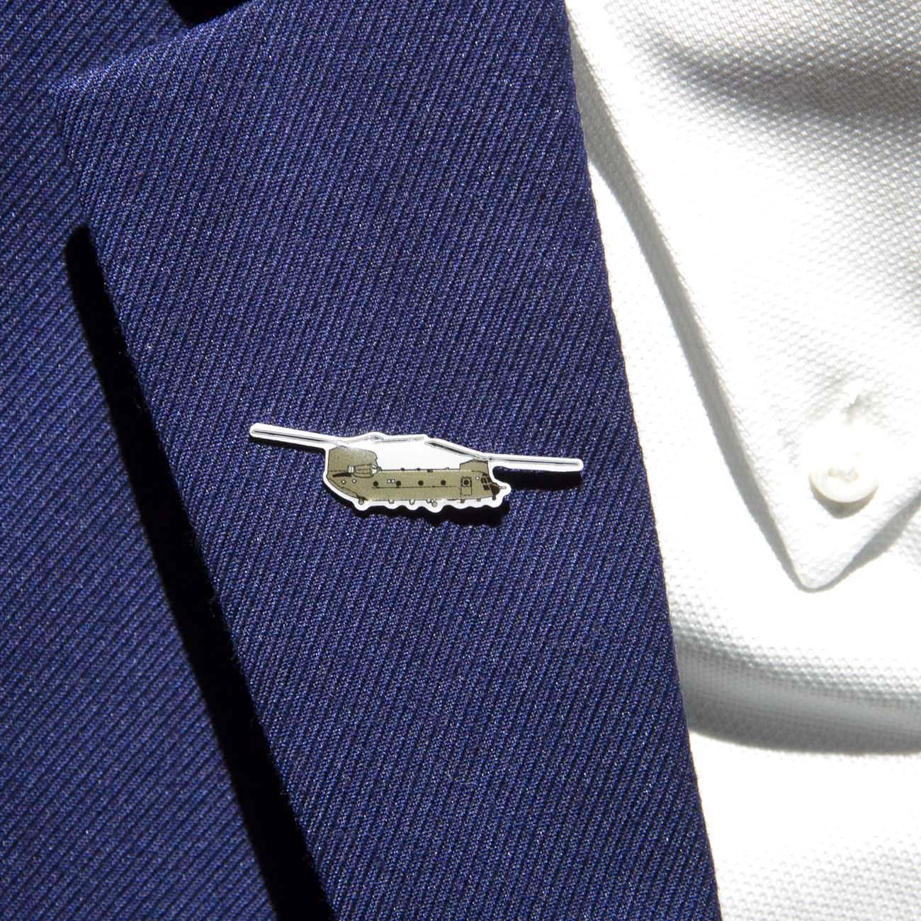 A close-up image displays a person wearing a textured navy blazer adorned with The Boeing Stores CH-47 Lapel Pin, shaped like an airplane. Paired with a white shirt featuring small buttons, the lighting emphasizes the blazers texture and enhances the pins epoxy-finished shine.
