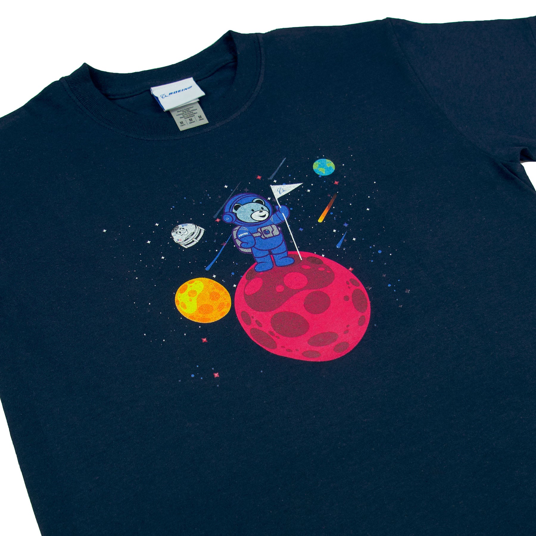 The Boeing Bear Kids T-Shirt from The Boeing Store features a navy blue design with a cartoon astronaut on a red planet, surrounded by yellow planets, a spaceship, and stars. The playful space scene captures the imagination of young Space Explorers as the astronaut waves a flag.