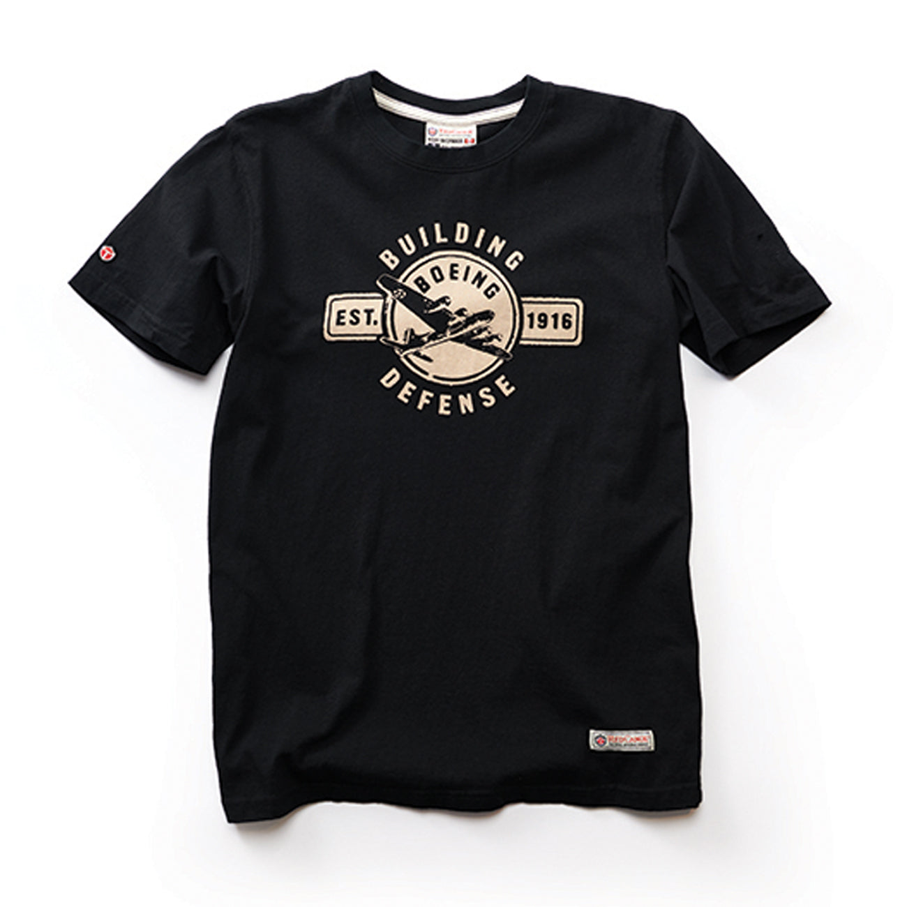 The Boeing Stores Red Canoe Boeing Defense T-Shirt is a black crew neck tee featuring a vintage-style Building Defense graphic with a WW2-era plane. It includes Boeing Defense and Est. 1916 in a badge design, ideal for aviation enthusiasts.