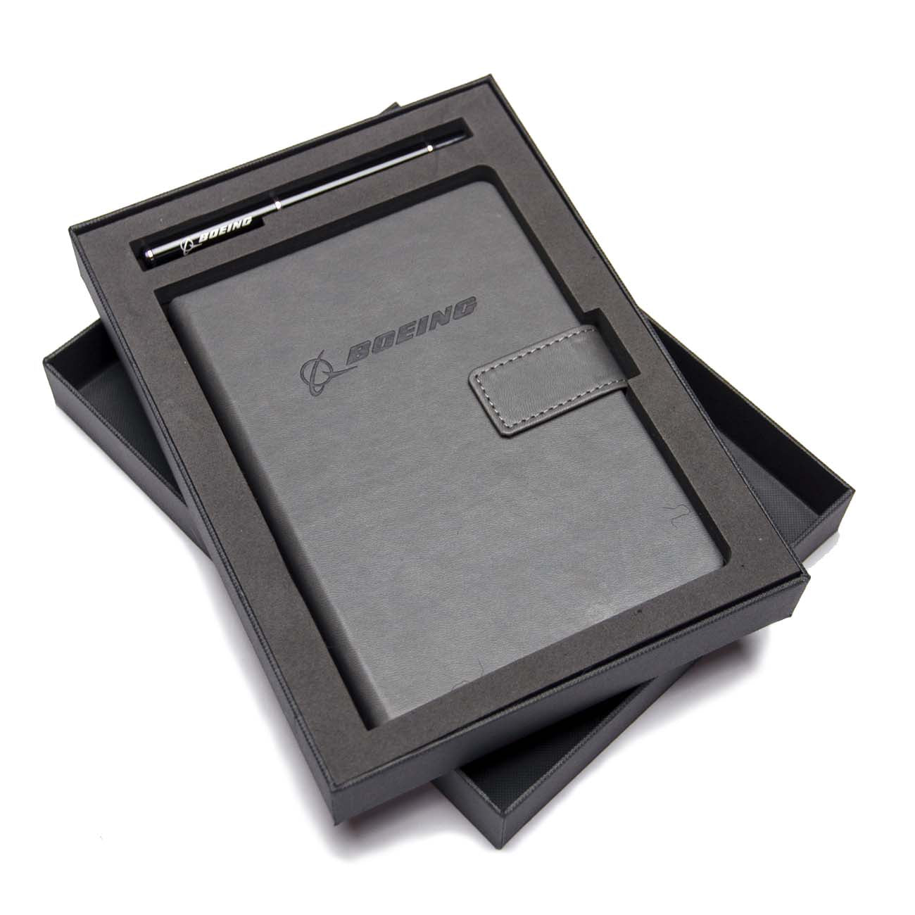 The Boeing Stores Boeing Notebook Pen Set includes a black leather notebook with a clasp and matching branded pen, elegantly arranged in a sleek gift box, with the lid partially open to reveal contents neatly placed on wood-free paper inside.