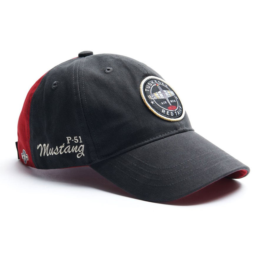 The Red Canoe Boeing Tuskegee Red Tails Hat by The Boeing Store is a black cap with red accents, featuring a round embroidered patch that says Tuskegee Airmen Red Tails and P-51 Mustang elegantly embroidered in white on the side.