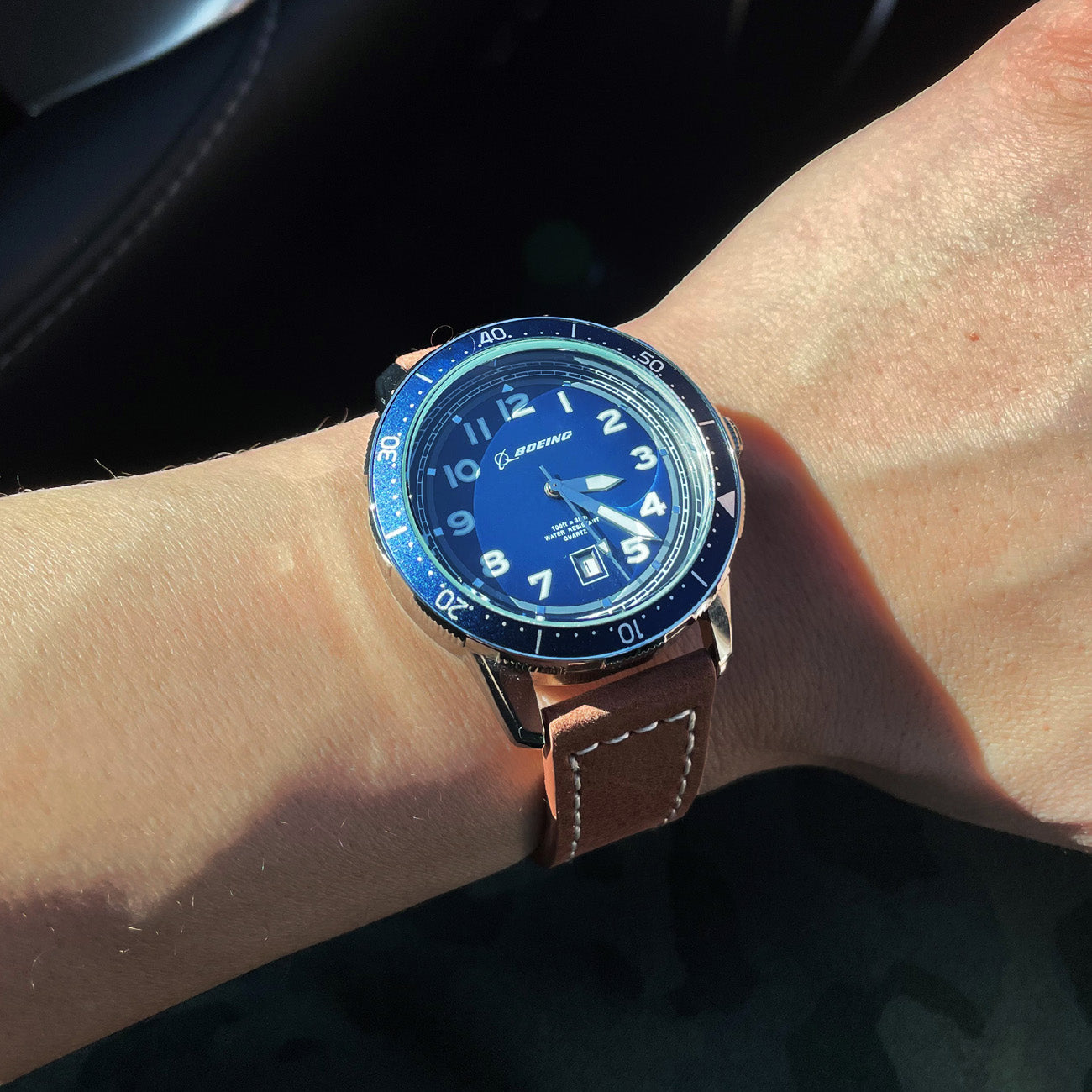 The Boeing Stores Boeing Brown Leather Watch features a blue dial with a silver bezel and Boeing logo. Its stainless steel case and brown leather strap shine in natural light, while the Japanese movement guarantees precise timekeeping.