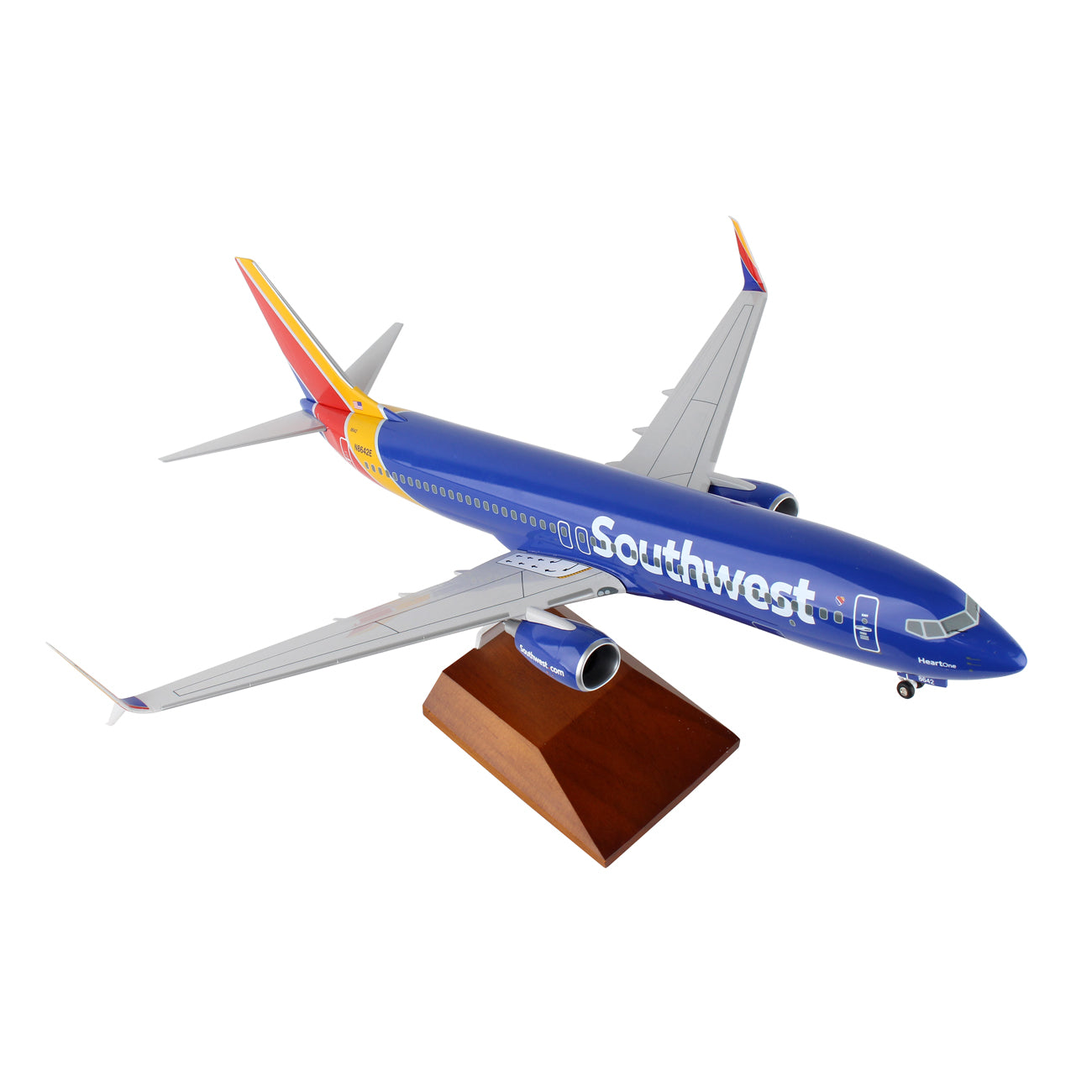 The Daron Southwest Airlines Boeing 737-800 1:100 Model rests on a wooden stand, featuring a sleek design with extended wings and tail. Its painted in blue with red, yellow, and orange accents and has detailed spinning engines.