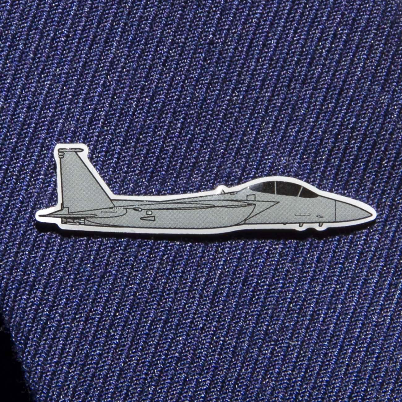 The Boeing Store presents the Boeing Illustrated F-15 Lapel Pin, a sleek gray fighter jet pin with black outlines and an epoxy finish. Its set against blue textured fabric, perfect for suits or ties.
