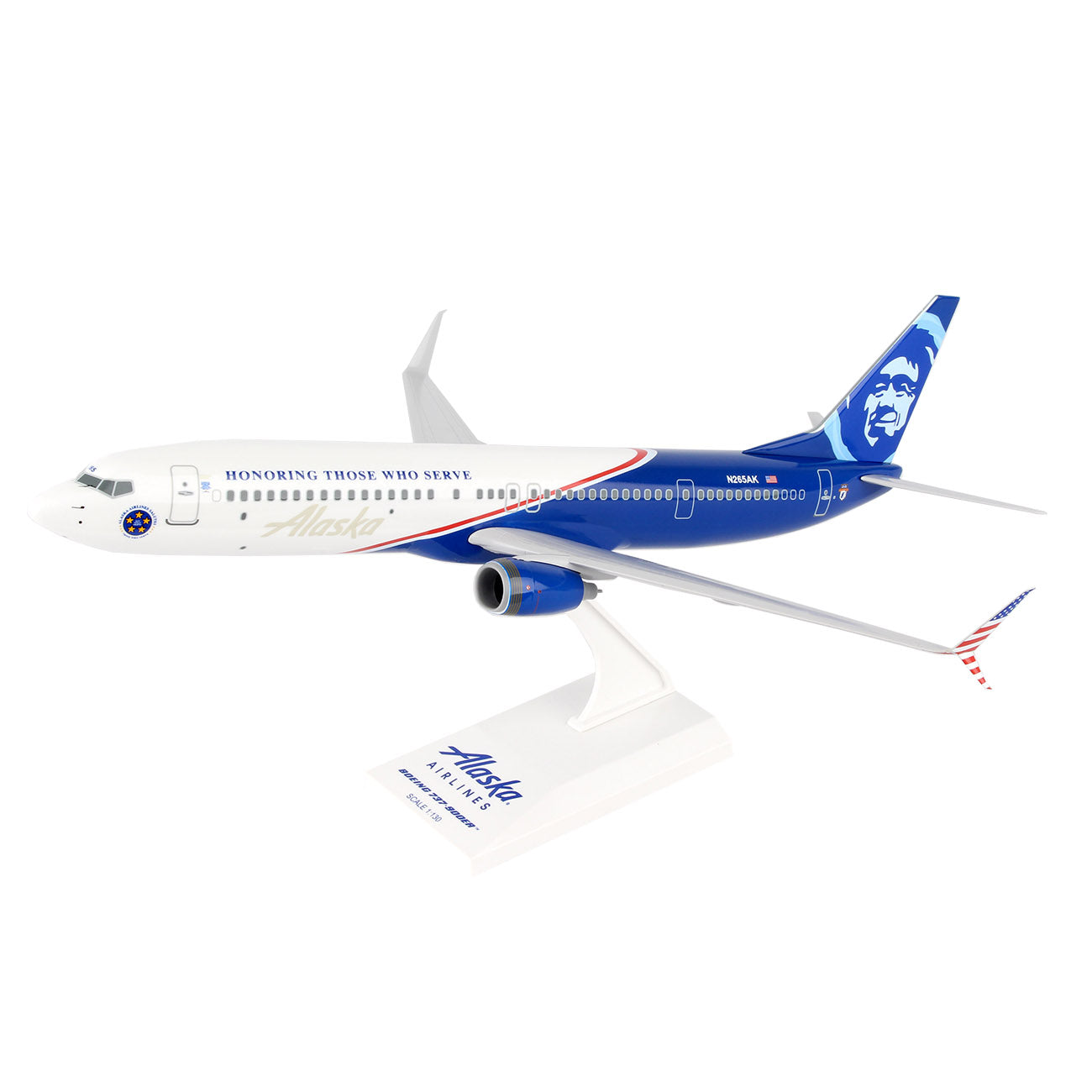 The Daron Alaska Airlines Boeing 737-900 Veterans 1:130 Model features red, white, and blue livery with HONORING THOSE WHO SERVE, the Alaska Airlines logo, a face on the tail, and comes mounted on a white display stand.